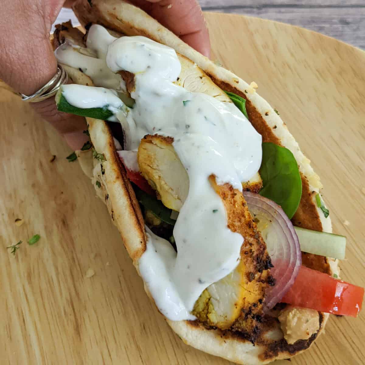 zhug feta hummus chicken wrap on a bamboo plate and folded in hand